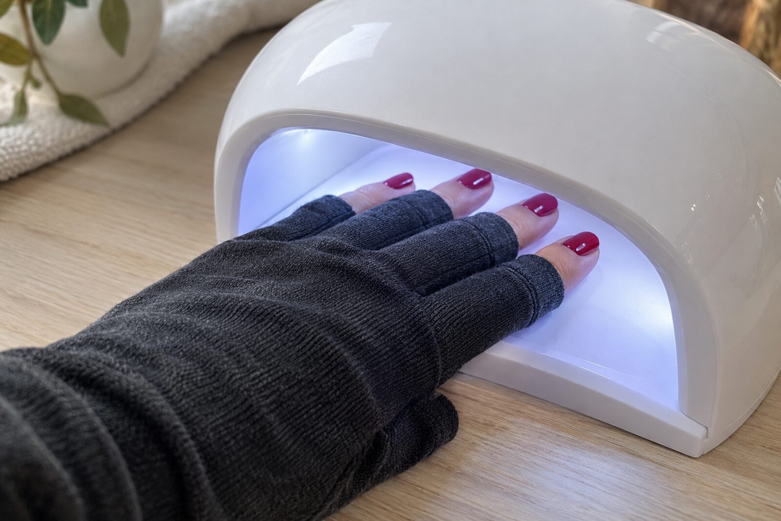 Hand met een donkere vingerloze handschoen in een nagellamp, alleen de vingertoppen met rode gellak vrij